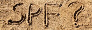 Sun protect factor (SPF) word written in sand on the beach with question mark.
